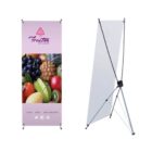 Two views of a purple fruit-themed banner stand. The front shows images of assorted fruits like grapes, pineapples, and apples, with the text Fruites by Lalas. The back image displays the stands supporting structure.