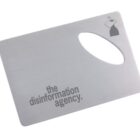 A metal card with an oval cutout features the text the disinformation agency in bold, black letters. A small illustration of a TV silhouette with a hat is in the top right corner.