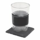 A glass cup with a black leather band around its middle sits on a square slate coaster. The cup contains a dark liquid, possibly coffee. The image has a white background.