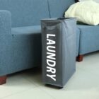 Grey laundry hamper on wheels beside a blue sofa.