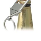 A close-up image of a bottle opener with a triangular handle resting on the cap of a brown beer bottle. The opener has a keyring attached, and the bottle cap is gold with red accents.