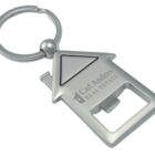 A silver keychain shaped like a house with a built-in bottle opener. It features the text Carl Anders Real Estate engraved on it.