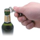 A hand using a bottle opener to remove the cap from a green glass bottle.