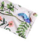 Close-up of fabric with a colorful design featuring green vines, pink flowers, and a blue butterfly. The stitching is visible along the edge of the fabric.