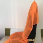 A chair is covered with a bright orange cloth draped over its back and seat. The chair is situated at a table, and the background features a plain, light-colored wall.