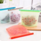 Reusable silicone food storage bags in various colors are displayed on a kitchen counter. Some bags contain items like vegetables and fruits. The bags have colored seals and one is placed on a wooden surface.