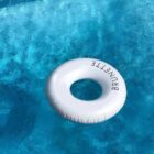 A white inflatable ring with the word BRUNETTE partially visible floats on clear blue pool water.