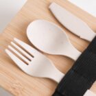 A set of eco-friendly cutlery, including a knife, spoon, and fork, made of beige biodegradable material, placed on a wooden surface. The utensils are secured with a black fabric strap.
