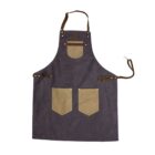 Dark blue apron with adjustable brown leather straps and brass rivets. It features one small chest pocket and two large front pockets in contrasting tan fabric, along with a metal ring on the left side for tools or accessories.