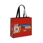 A red tote bag featuring a stylized design of a bowl with cereal. The text on the bag says Tweedle Meals. The bag has black handles and decorative elements in orange and yellow tones.