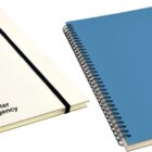 Two spiral-bound notebooks with elastic closures. One is white, and the other is blue. Both have the water agency logo featuring a water droplet on the cover.