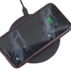 A smartphone with a red case is placed on a black wireless charging pad. The phone screen displays a battery icon indicating it is 53% charged. The charging pad is connected to a cable.