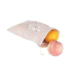 A beige cloth bag with a floral pattern is slightly open, revealing an orange and a peach partially outside. The bag has a drawstring closure. The background is plain white.