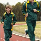 Father and son jogging on a track, both wearing matching green and yellow tracksuits. They are smiling and running together in an outdoor setting with trees in the background. The word SPORTS is at the bottom of the image.