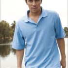 Man wearing a light blue polo shirt walking near a calm body of water, with trees and a cloudy sky in the background. The word CASUAL is written in large white letters at the bottom.