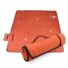An orange picnic blanket with a floral pattern, partially rolled up with a handle for carrying. The brand logo is visible in the corner.