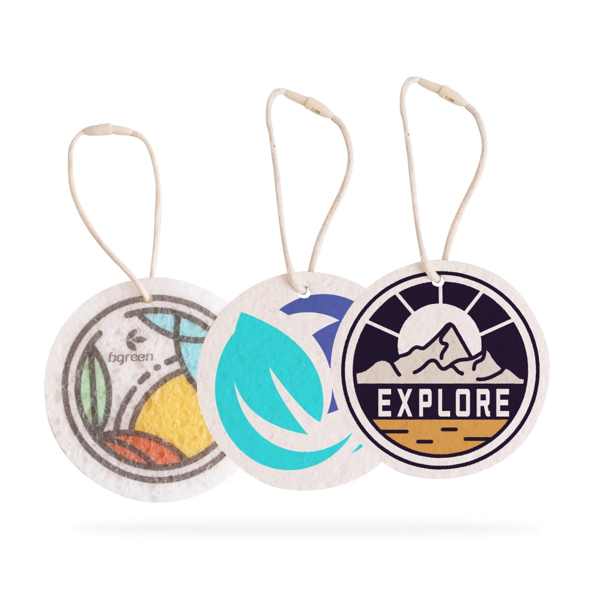 Three circular air fresheners with strings. The first shows colorful stylized leaves and oranges, labeled bgreen. The second features a blue leaf design. The third has a mountain scene with the word EXPLORE beneath.