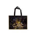 A black tote bag featuring the design of a clock with golden numbers, the Disney Classic logo, and text in Japanese. The time on the clock reads midnight, and there are sparkles around the design. The handles are black.
