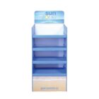 Blue retail display stand with four shelves and a header featuring the sun zone logo. The bottom section includes a website URL. The stand is empty, with a beach sand and sky design at the base.