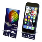 A smartphone rests on a clear plastic stand displaying its home screen. Next to it is a card featuring a colorful pattern with the text action not words! along with a website and phone number.