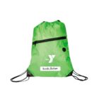 A green drawstring backpack with a black zipper pocket. It features a white logo with the letter Y and the text the. Below is a name label with Ursula Hudson. Black drawstrings and reinforced corners are visible.