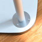 A vertical metal pole attached to a rectangular base with screws. The base has rounded corners and rests on a wooden surface with visible grain patterns.