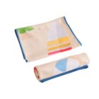 A folded beige baby blanket with blue edges, featuring colorful designs of a surfboard, palm tree, and beach ball. Another blanket, rolled up, is placed in front of the folded one.