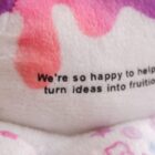 Close-up of a plush toy with pink and purple patterns. The text on the plush reads, Were so happy to help turn ideas into fruition.