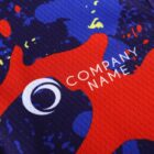 Close-up of a colorful abstract design on a fabric surface, featuring splashes of red, blue, and yellow. The words COMPANY NAME are printed in white on the red area.
