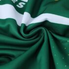 Close-up of green fabric with a spiral gather at the center. The fabric is patterned with white and yellow designs, including text partially visible in the upper left.