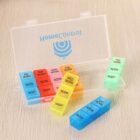 A weekly pill organizer with compartments labeled by day and time: Friday to Monday in shades of blue and red, Tuesday to Thursday in yellow and green, and Saturday and Sunday in blue. The lid is open, displaying the word HOLWESOUFLOR.