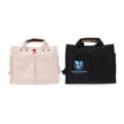 Two canvas tote bags are displayed side by side. The left bag is beige with a red heart logo and the word Ecobee below it. The right bag is black with a turquoise leaf logo and the text GreenChoice underneath. Both have brown handles.