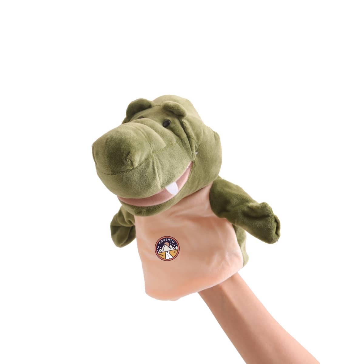 A person is holding a green dinosaur puppet. The puppet has a friendly expression with round eyes and a wide mouth. It is wearing a beige shirt with a small logo featuring a triangular design. The background is plain white.