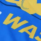 Close-up of a blue and yellow fabric with large yellow letters, partially displaying the word WASH. The design features a mix of bold, curved elements.