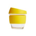 A clear glass cup with a yellow silicone band around its center and a yellow lid on top. The lid and band have a smooth, matte finish. The cup is empty and isolated on a plain white background.