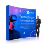 A man in a suit stands beside a promotional display featuring a person wearing virtual reality goggles. The sign reads Technology Innovation, Discount Up to 30% Off with filler text and a logo.