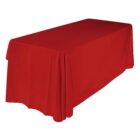 A rectangular table is covered with a plain, vibrant red tablecloth that hangs evenly over the edges, cascading to the floor. The background is a simple white or light color, emphasizing the tablecloths bold hue.