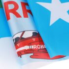 Close-up of a colorful printed fabric showing part of a red airplane with the word ROYAL on it, a large white star against a blue background, and red block letters partially visible on a white area.