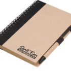 A spiral-bound notebook with a brown cover and black band. It has Sink Em Swimwear printed on the front. A pen is attached to the side using a black elastic loop.