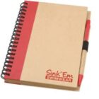 Spiral-bound notebook with a red and tan cover featuring SinkEm Swimwear logo in the bottom right corner. A red and tan pen is clipped to the right side of the notebook.