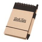 A small spiral-bound notebook with a brown cover and a black band, featuring the text Sink Em Swimwear. A pen is attached to the side of the notebook with an elastic loop.