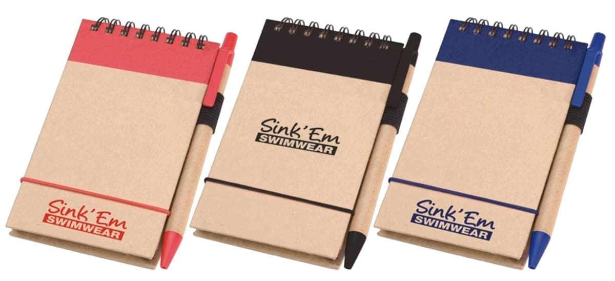 Three small notepads with spiral bindings and attached pens. Each has a different color scheme: red, black, and blue. The covers display the text Sink Em Swimwear.