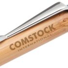 Close-up of a pen with a bamboo finish and a metal clip. The pen is engraved with the text COMSTOCK INTERNATIONAL on the side. The tip is partially visible.