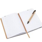 An open notebook with lined pages and a date header sits on a white surface. A pen with a beige body and black accents rests diagonally across the pages. A light brown ribbon bookmark is seen between the pages.