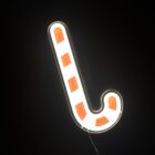 A glowing candy cane neon sign with alternating red and white stripes is lit against a dark background, illuminating its surroundings.