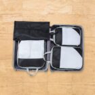 An open suitcase with four neatly packed black and white travel packing cubes, arranged on a wooden floor. The cubes have mesh panels and handles, optimizing the luggage space efficiently.