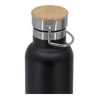 A close-up of the top of a black insulated bottle featuring a smooth wooden cap and a metal loop handle. The bottle has a sleek design, combining metal and natural elements.