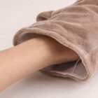 A hand is partially inside a soft, brown, furry mitt, possibly for warmth or cleaning, on a light surface.