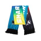 A colorful sports scarf displaying the word SHARK in large white letters. The scarf features a gradient design with blue, green, yellow, and black sections, adorned with a shark logo, and finished with black fringes at the ends.