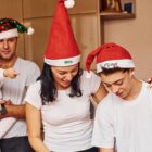 A group of four people, including a baby, enjoy a festive moment indoors. Two of them wear red Santa hats. The atmosphere is cheerful and familial. Everyone is dressed in casual white shirts.
